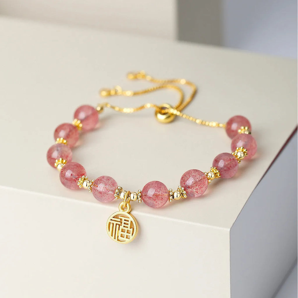 Close-up of a women's adjustable bracelet with pink strawberry quartz crystal beads and a silver fu charm on a geometric chain.