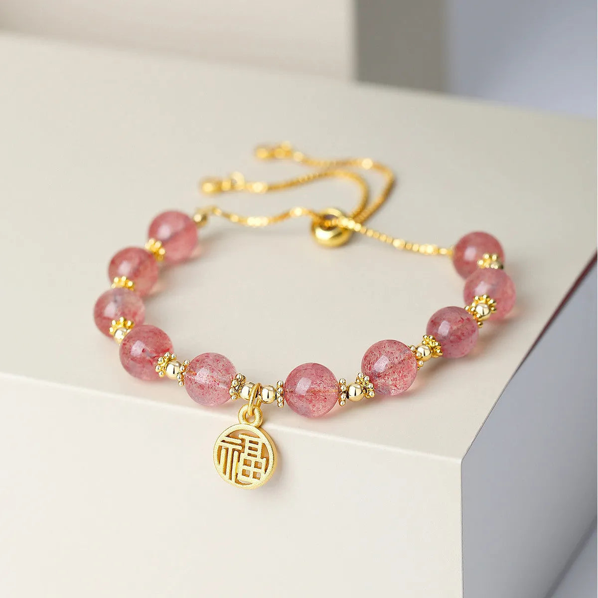 Close-up of a women's adjustable bracelet with pink strawberry quartz crystal beads and a silver fu charm on a geometric chain.