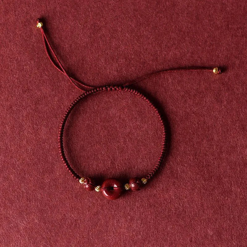 Traditional cinnabar bracelet with a heart-shaped peace buckle clasp on a red rope.