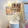 Teddy bear cartoon LED night light with acrylic shade on a table, USB cable attached