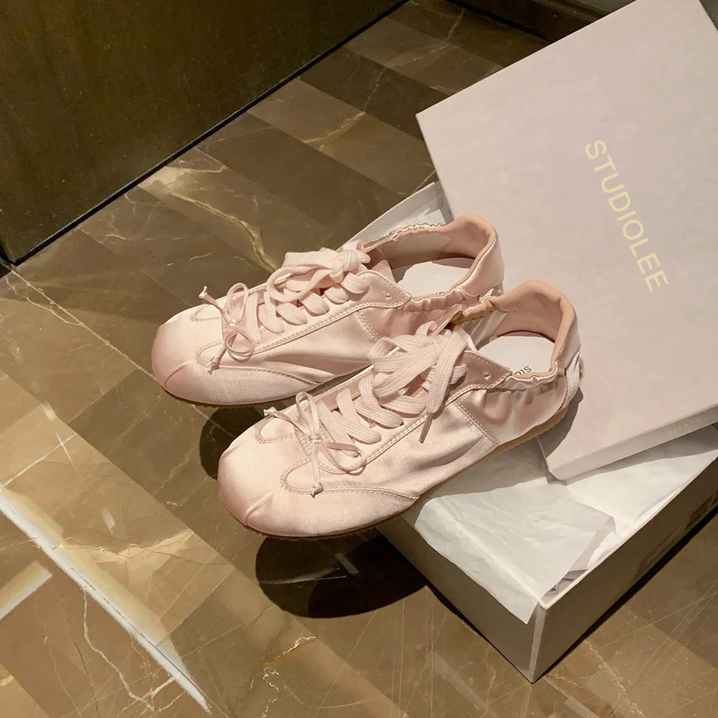 Women's champagne pink satin ballet flats with round toe and lace-up front, shown on a white background.