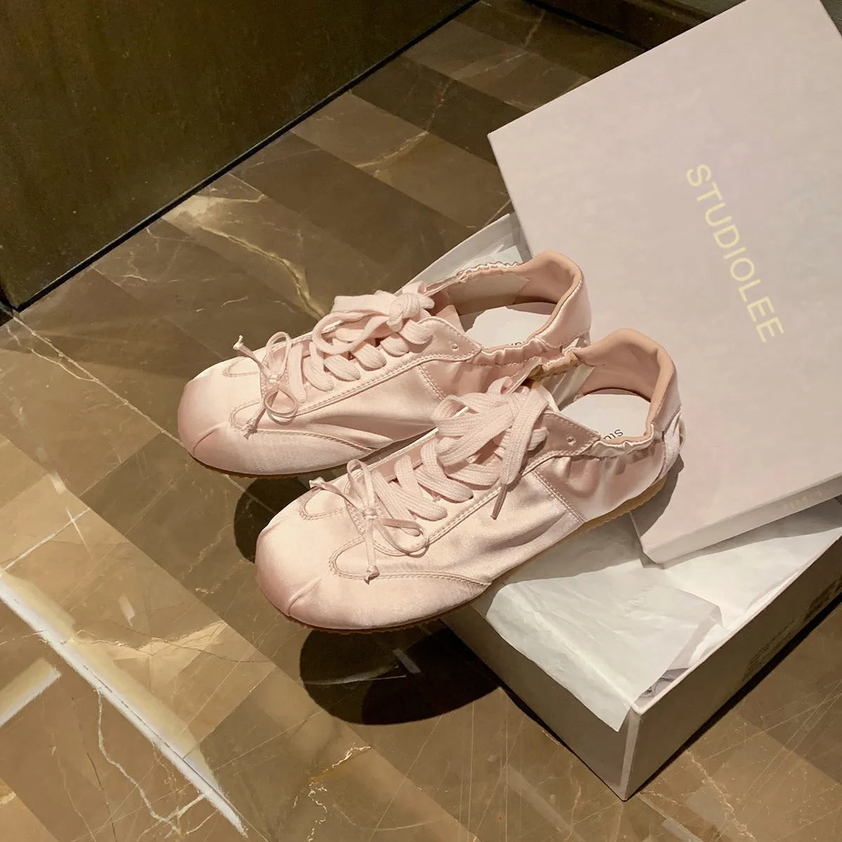Women's champagne pink satin ballet flats with round toe and lace-up front, shown on a white background.