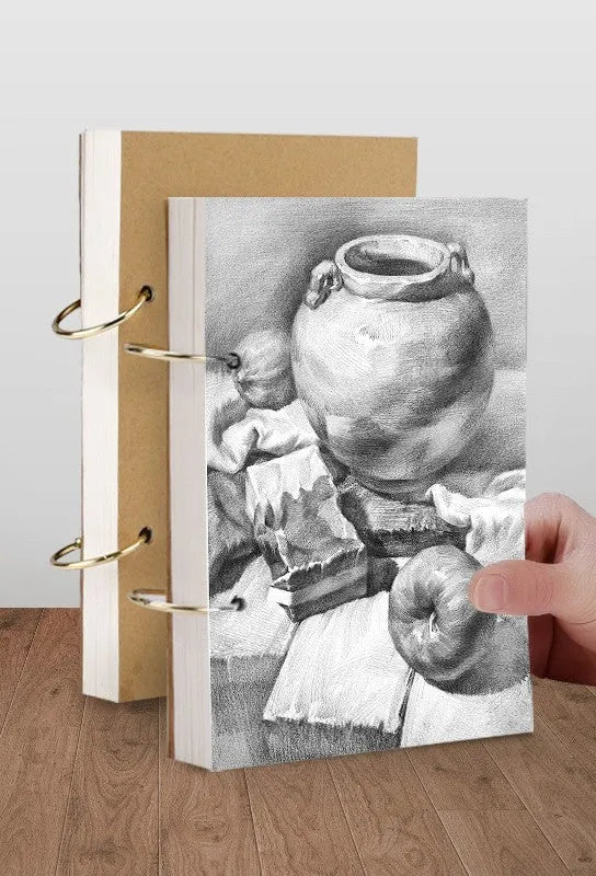 8K thickened sketchbook open on a table with marker drawings, showing linen and black card cover options.