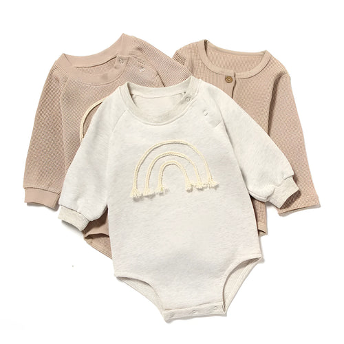 Long-sleeved waffle cotton baby romper in a neutral colour on a hanger, showing the triangular climbing front closure.