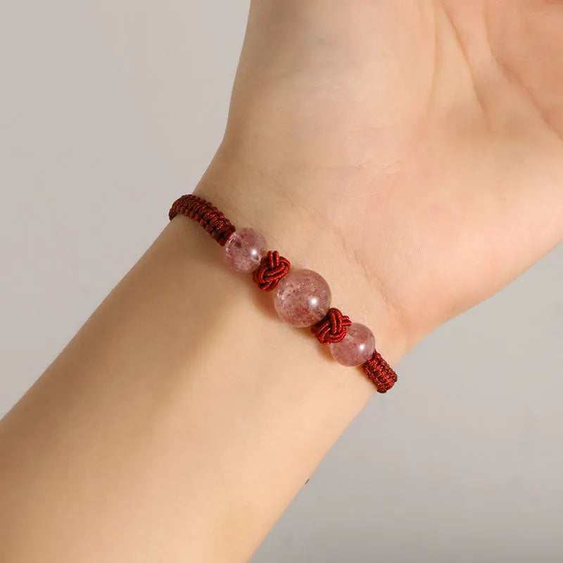 Woven red rope bracelet with a spherical strawberry quartz bead and alloy clasp.