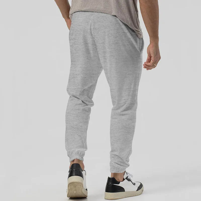 Man wearing grey loose tapered cotton blend track sweatpants with a straight leg.