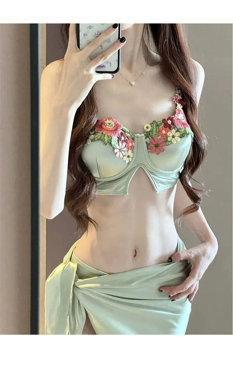 Green women's three-piece bikini set with triangle top, briefs, and skirt on hanger